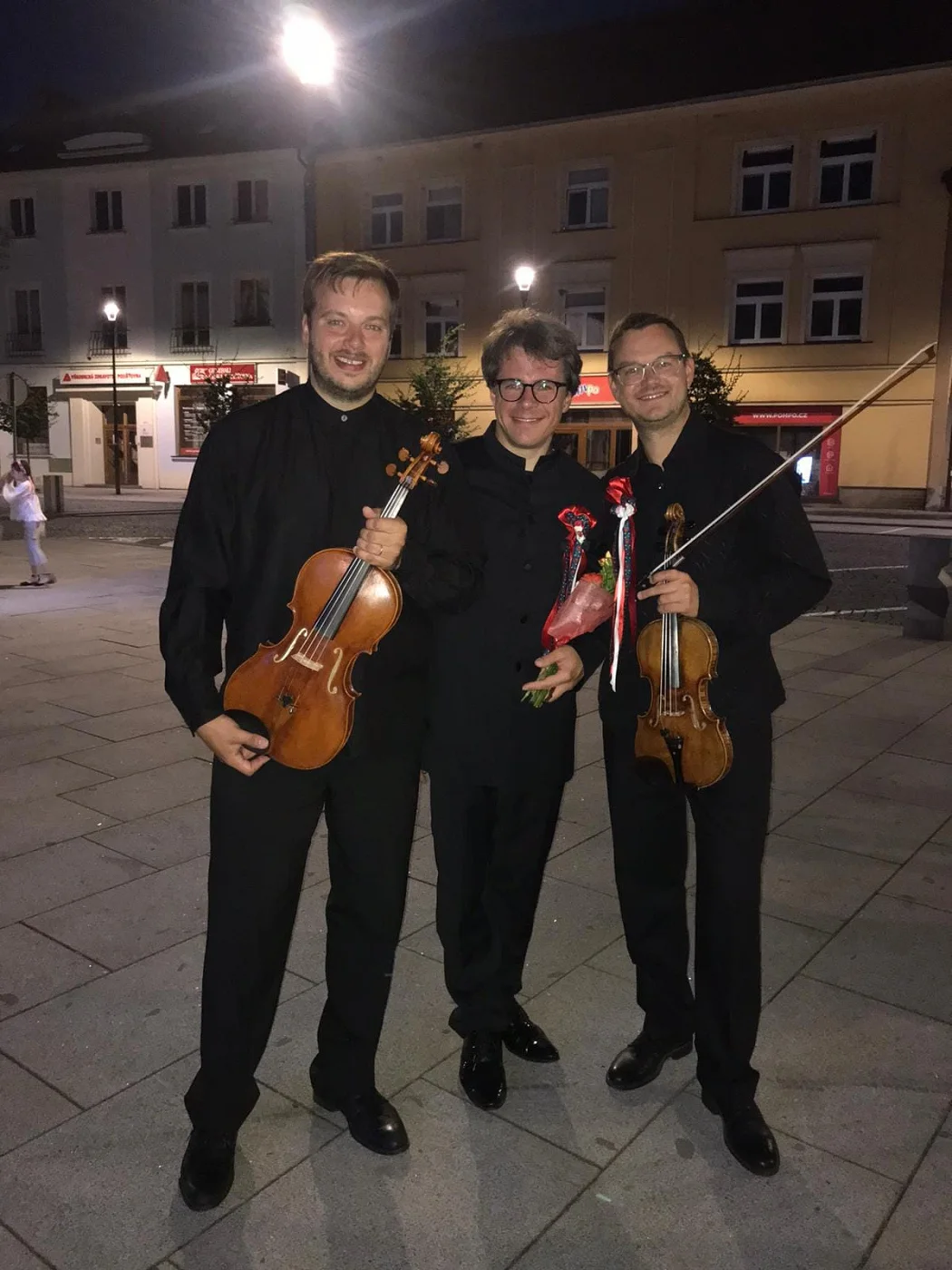 Three musicians with their instruments on a town square at night