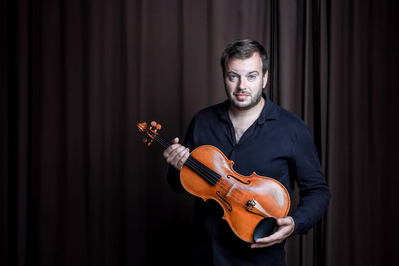 Jiří Kabát holding his viola in front of a brown curtain